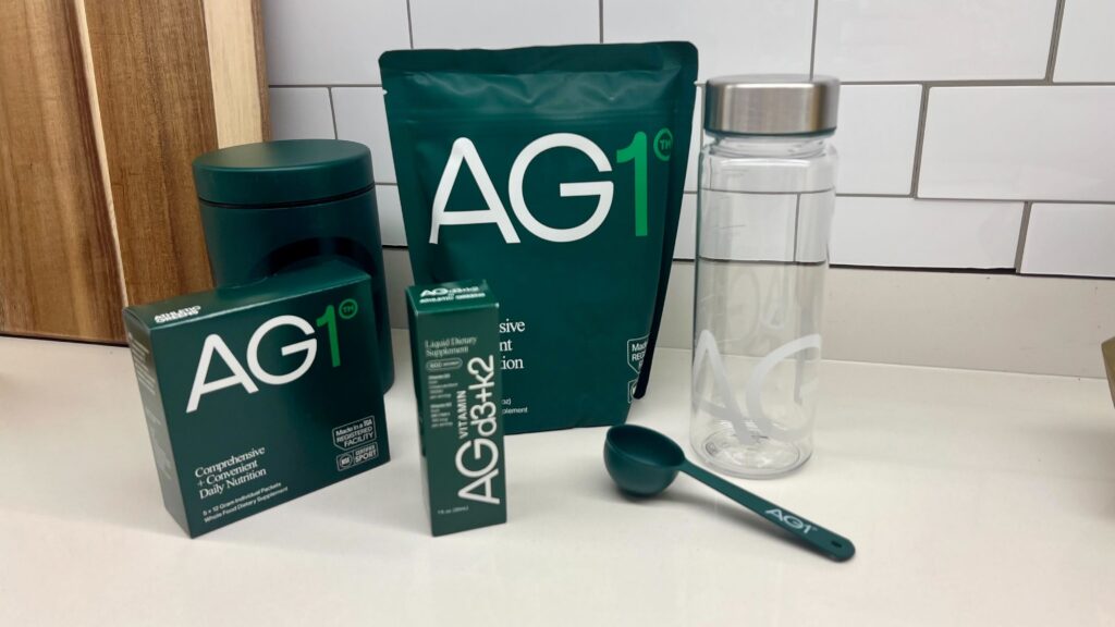 Athletic Greens AG1 pouch and travel pack sachets on a wooden counter with measuring spoon.