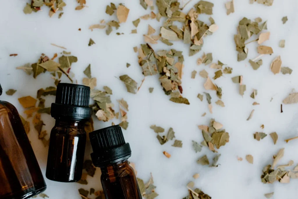 Glass essential oil bottles surrounded by dried herbal leaves on white background