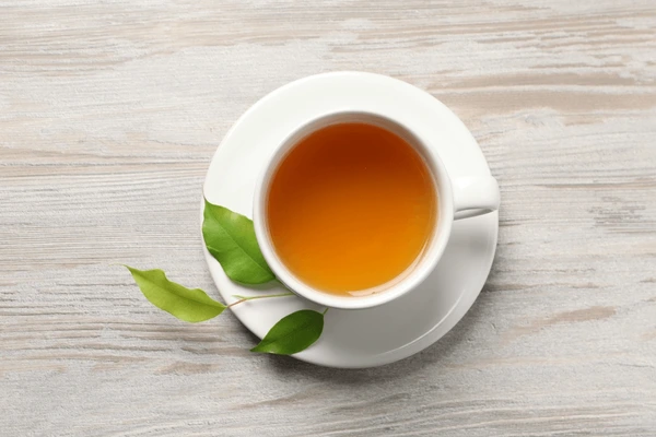 Top‑down view of a white cup filled with green tea on a minimalist wooden surface