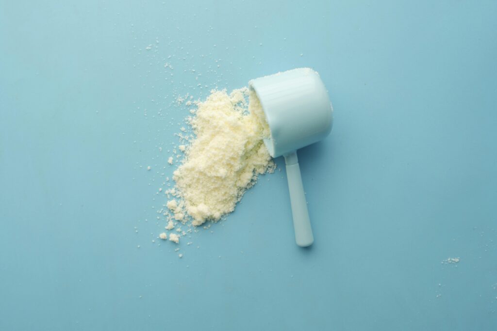 “High-quality white protein powder spilled from a scoop on a vibrant blue background — symbolizing clean nutrition, fitness supplements, and muscle recovery support”