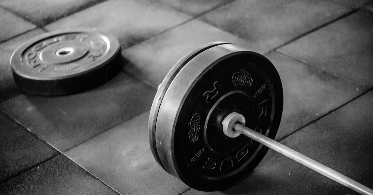 Grayscale image of heavy gym barbell and weights on rubber mat flooring.